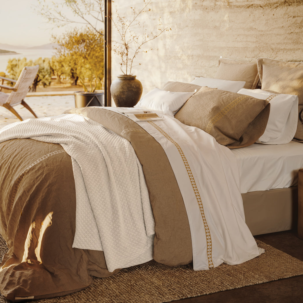 Cama vestida con textiles Alba, bordados geométricos y cojines en una habitación con luz natural.