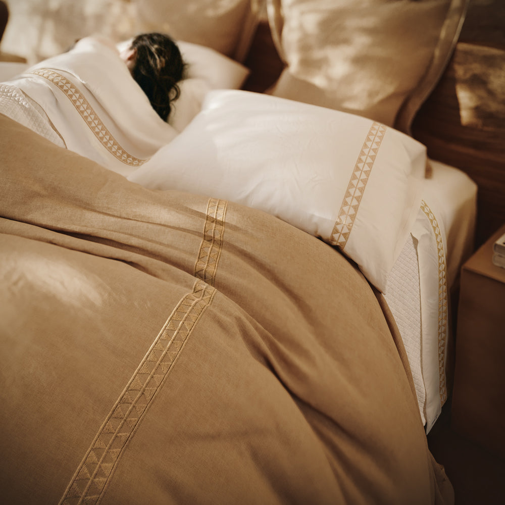Detalle de la cama Alba con bordado geométrico, fundas de almohada y textiles en tonos naturales.
