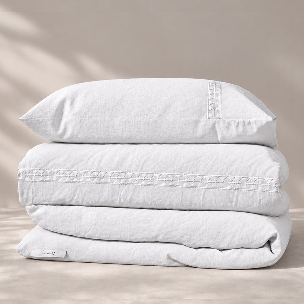 Funda Duvet Alba de lino misto blanco con bordado geométrico tono a tono y fundas de almohada, presentada doblada.