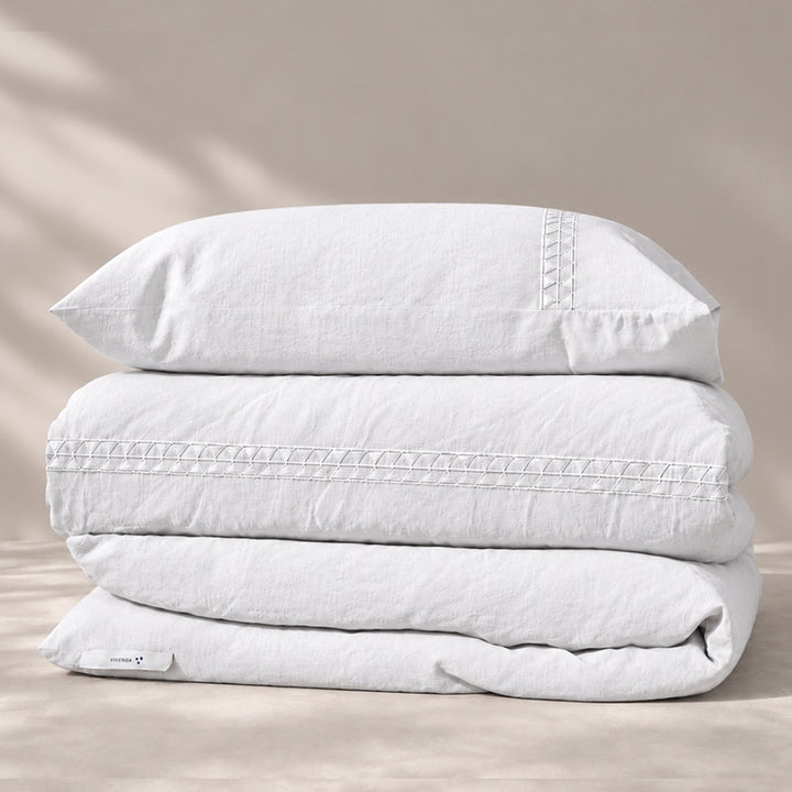 Funda Duvet Alba de lino misto blanco con bordado geométrico tono a tono y fundas de almohada, presentada doblada.