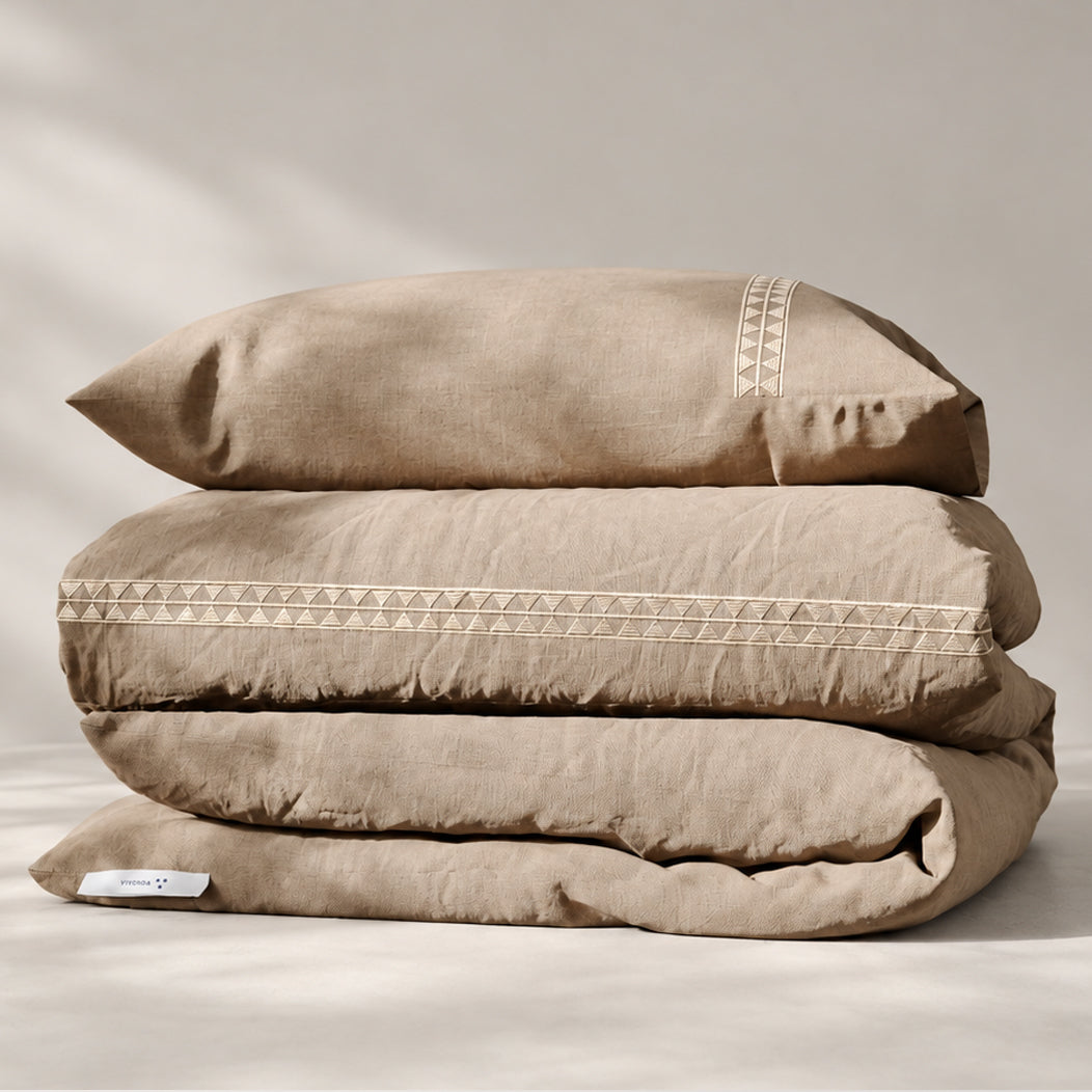 Funda Duvet Alba de lino misto natural con bordado geométrico tono a tono y fundas de almohada, presentada doblada.