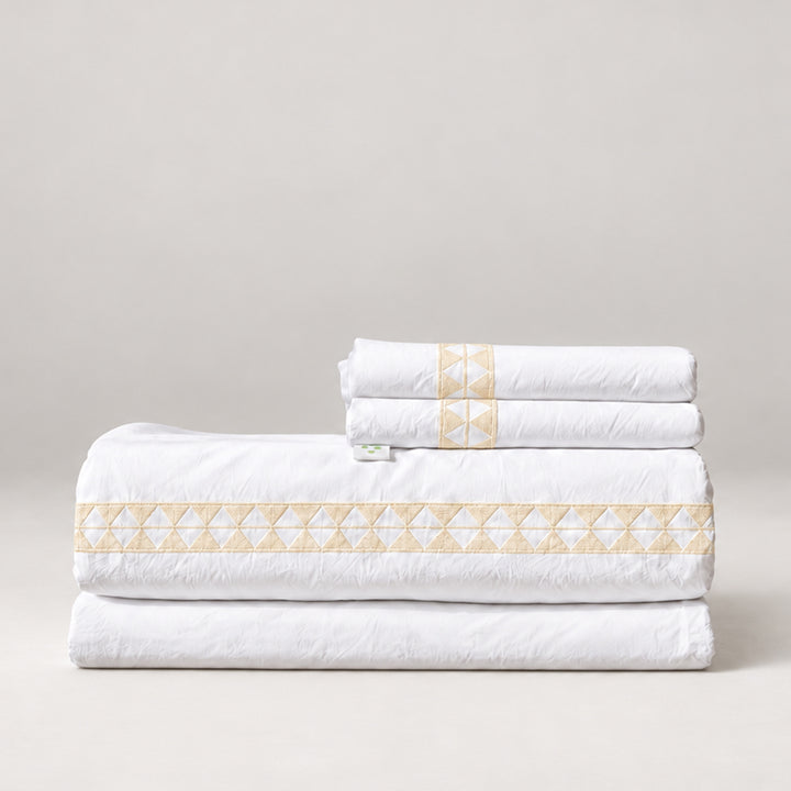 Juego de Sábanas Alba blanco con bordado crudo y fundas de almohada, presentado doblado.