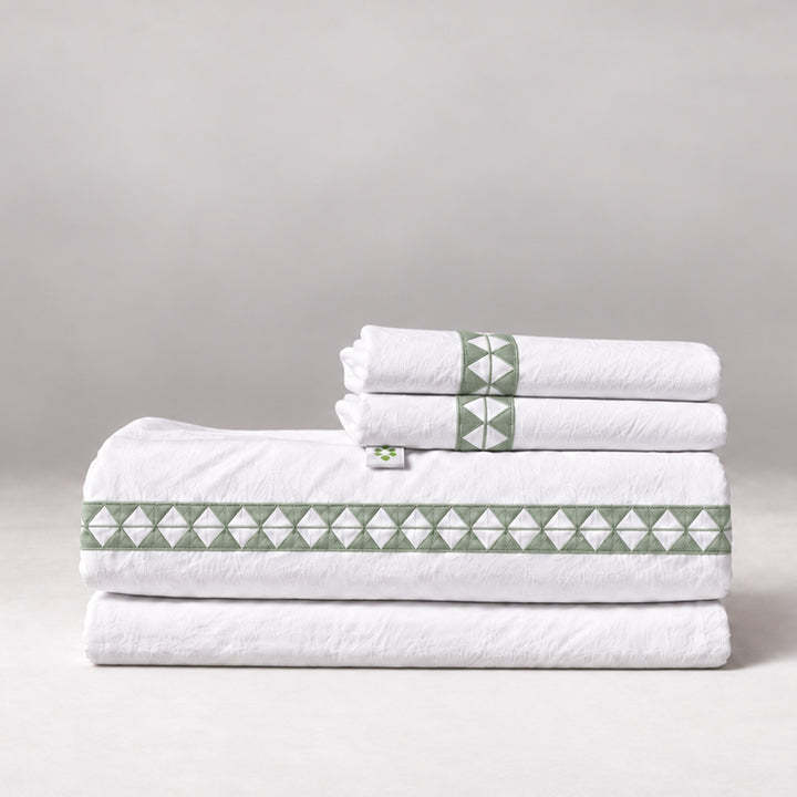 Juego de Sábanas Alba blanco con bordado laurel y fundas de almohada, presentado doblado.
