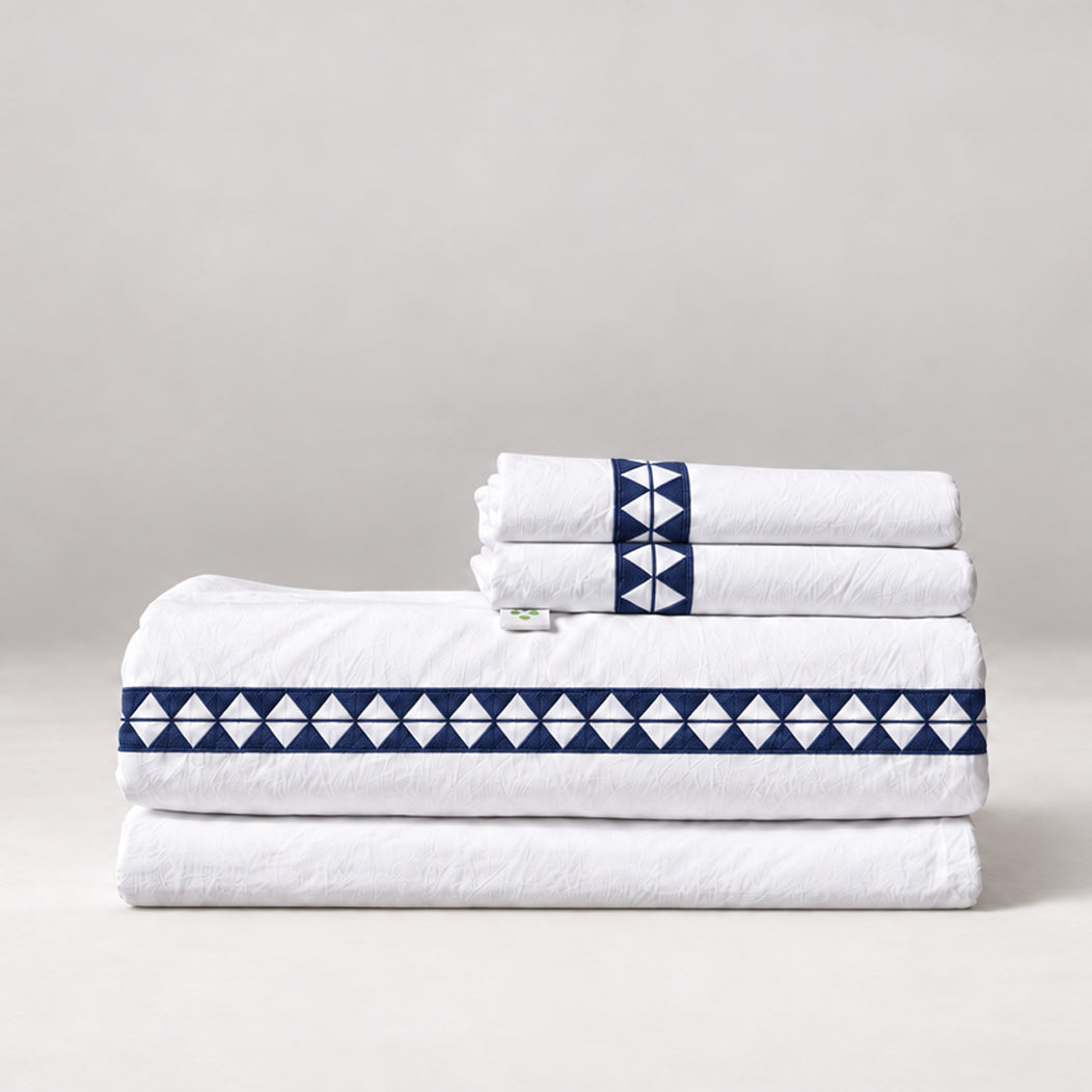 Juego de Sábanas Alba blanco con bordado marino y fundas de almohada, presentado doblado.