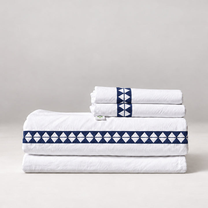 Juego de Sábanas Alba blanco con bordado marino y fundas de almohada, presentado doblado.