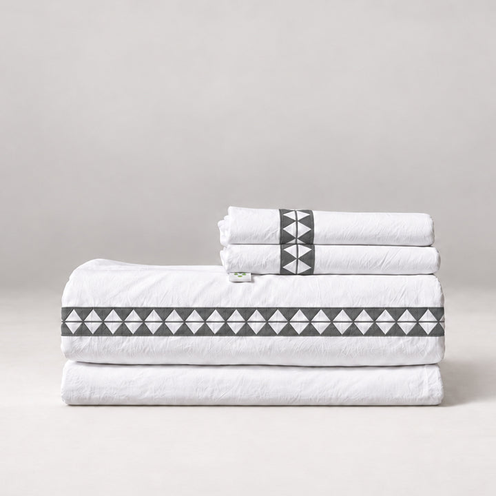Juego de Sábanas Alba blanco con bordado noche y fundas de almohada, presentado doblado.