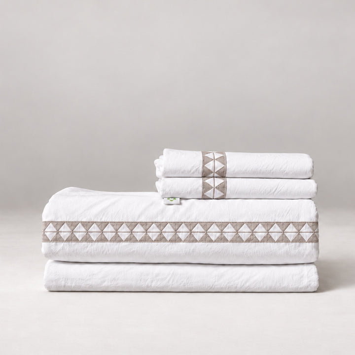 Juego de Sábanas Alba blanco con bordado olmo y fundas de almohada, presentado doblado.
