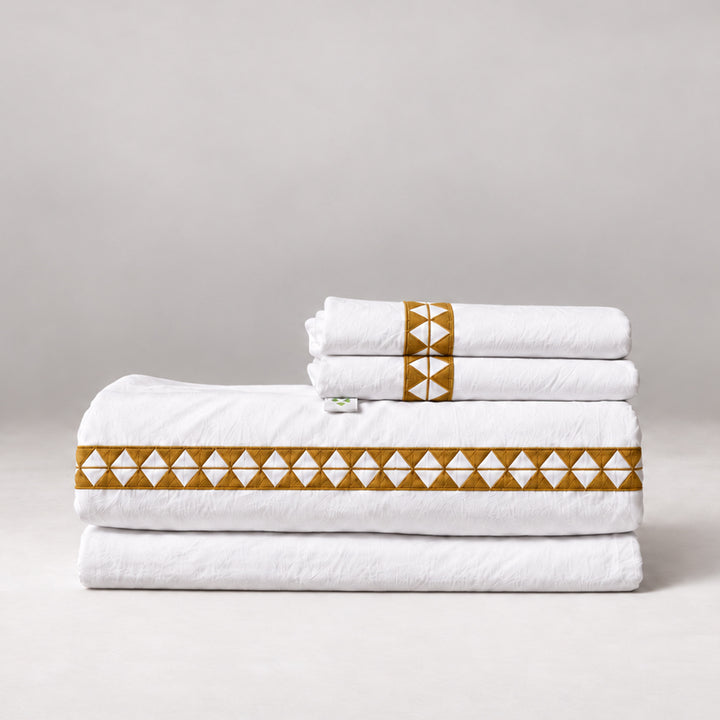 Juego de Sábanas Alba blanco con bordado sunset y fundas de almohada, presentado doblado.