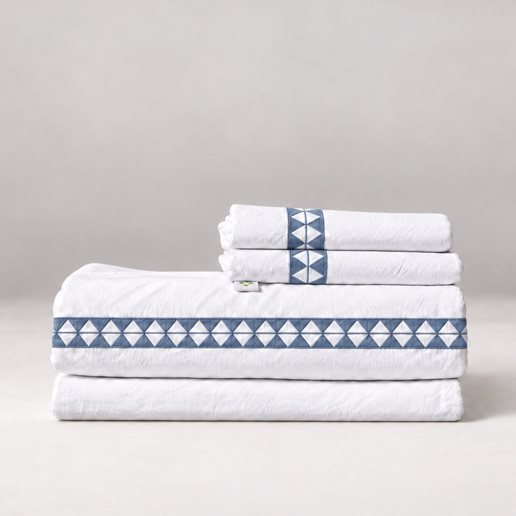 Juego de Sábanas Alba blanco con bordado zen y fundas de almohada, presentado doblado.
