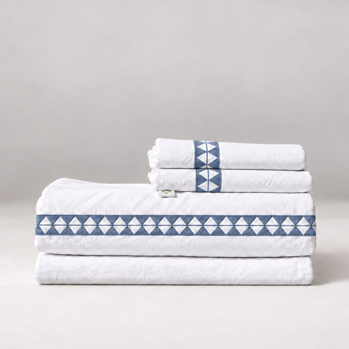 Juego de Sábanas Alba blanco con bordado zen y fundas de almohada, presentado doblado.