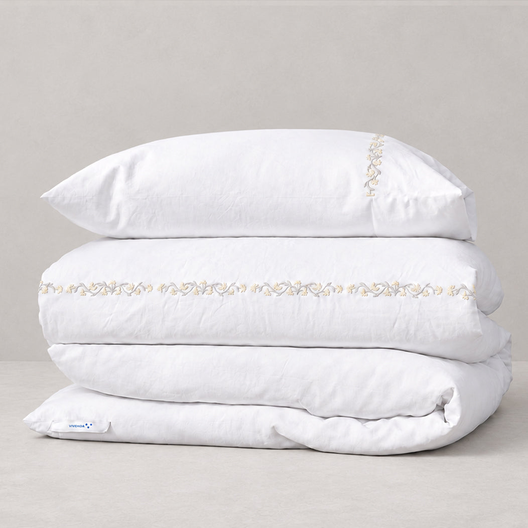 Funda Duvet Chicori de algodón percal blanco con bordado floral Crudo+Bruma y fundas de almohada, presentada doblada.