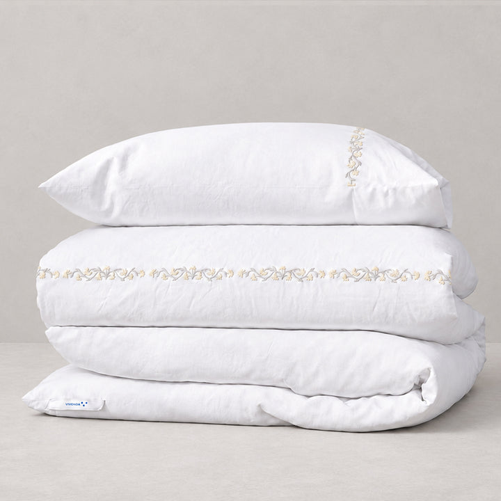 Funda Duvet Chicori de algodón percal blanco con bordado floral Crudo+Bruma y fundas de almohada, presentada doblada.