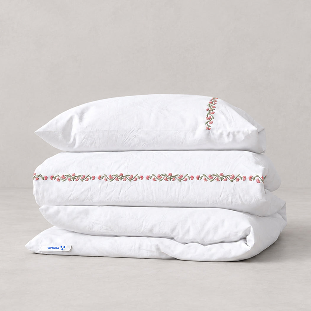Funda Duvet Chicori de algodón percal blanco con bordado floral Rosa+Laurel y fundas de almohada, presentada doblada.
