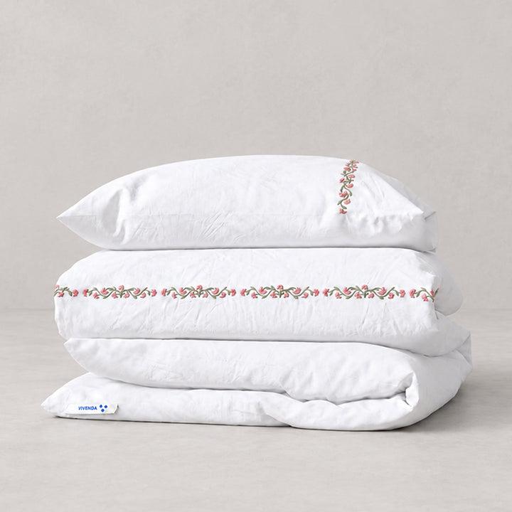 Funda Duvet Chicori de algodón percal blanco con bordado floral Rosa+Laurel y fundas de almohada, presentada doblada.