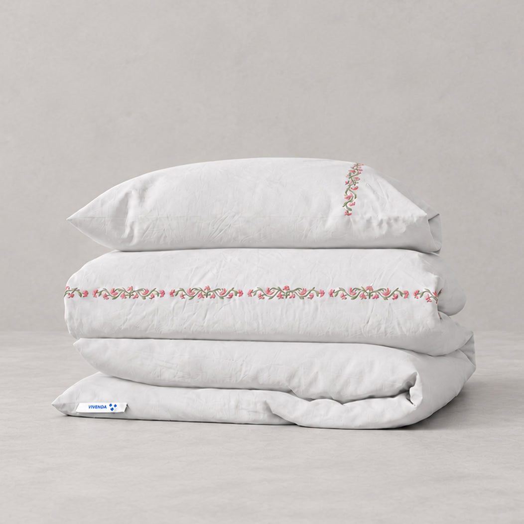 Funda Duvet Chicori de algodón percal blanco con bordado floral Rosa+Laurel y fundas de almohada, presentada doblada.