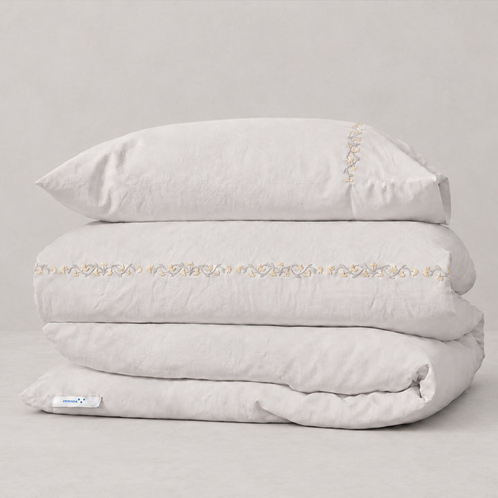 Funda Duvet Chicori de algodón percal bruma con bordado floral Crudo+Bruma y fundas de almohada, presentada doblada.