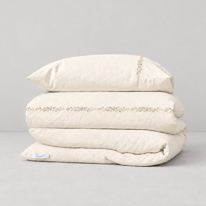 Funda Duvet Chicori de algodón percal crudo con bordado floral Crudo+Bruma y fundas de almohada, presentada doblada.