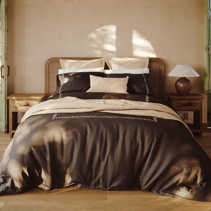 Detalle de la cama Chicori con bordado floral Crudo+Bruma, fundas de almohada y textiles en capas.