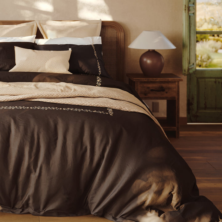 Detalle de la cama Chicori con bordado floral Crudo+Bruma, fundas de almohada y textiles en capas.