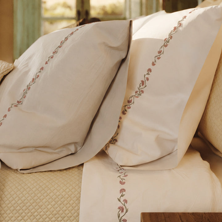 Detalle de la cama Chicori con bordado floral Rosa+Laurel, fundas de almohada y textiles en capas.
