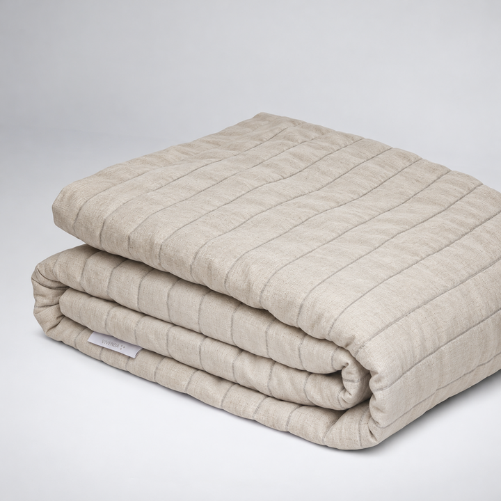 Coverlet Monte de lino en tono Natural, acolchado y doblado.