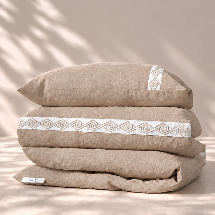 Funda Duvet Senda de lino misto Natural con tiras blancas bordadas en espiral y fundas de almohada, presentada doblada.