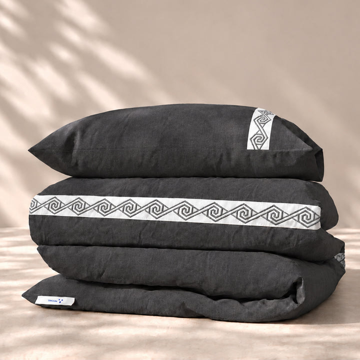 Funda Duvet Senda de lino misto Noche con tiras blancas bordadas en espiral y fundas de almohada, presentada doblada.