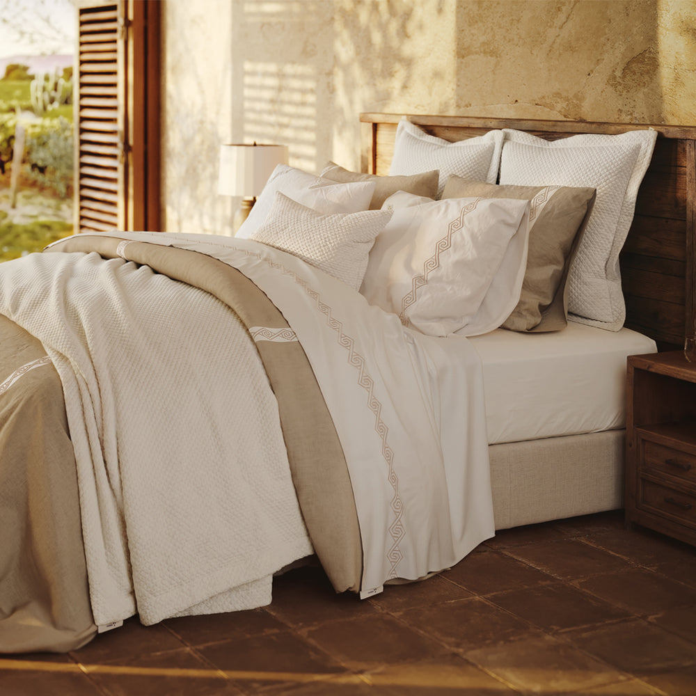 Cama vestida con Senda: detalle de tiras blancas con bordado en espiral sobre lino Natural y fundas de almohada.