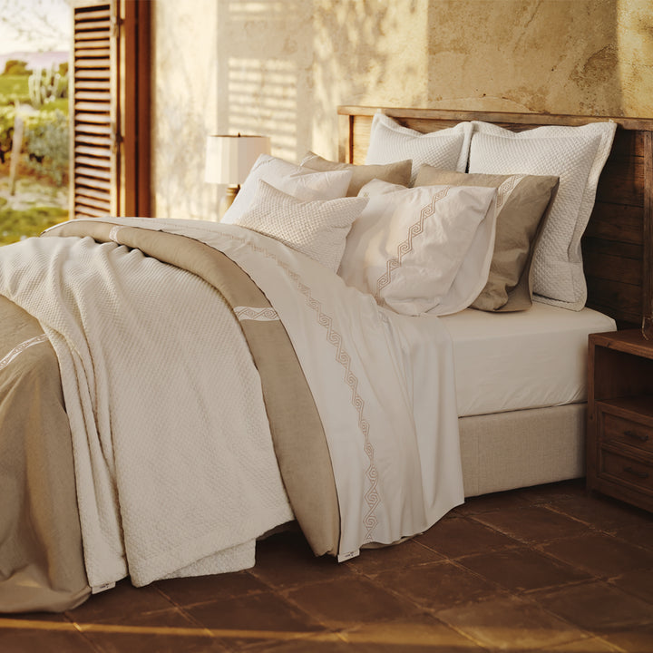 Cama vestida con Senda: detalle de tiras blancas con bordado en espiral sobre lino Natural y fundas de almohada.
