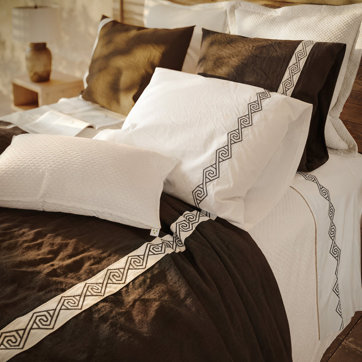 Cama vestida con Senda: detalle de tiras blancas con bordado en espiral sobre lino Noche y fundas de almohada.