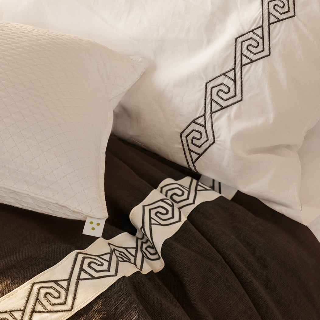 Cama vestida con Senda: detalle de tiras blancas con bordado en espiral sobre lino Noche y fundas de almohada.