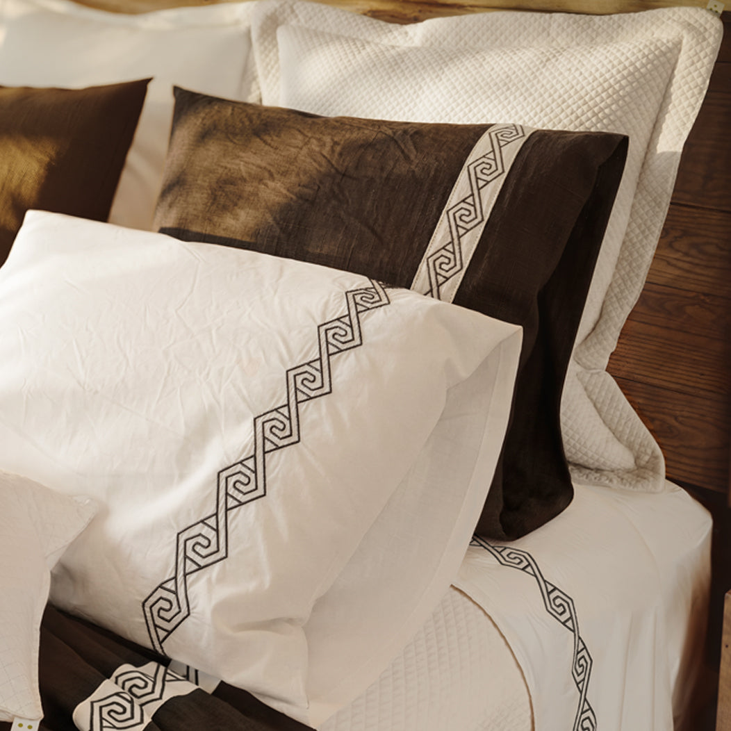 Cama vestida con Senda: detalle de tiras blancas con bordado en espiral sobre lino Noche y fundas de almohada.