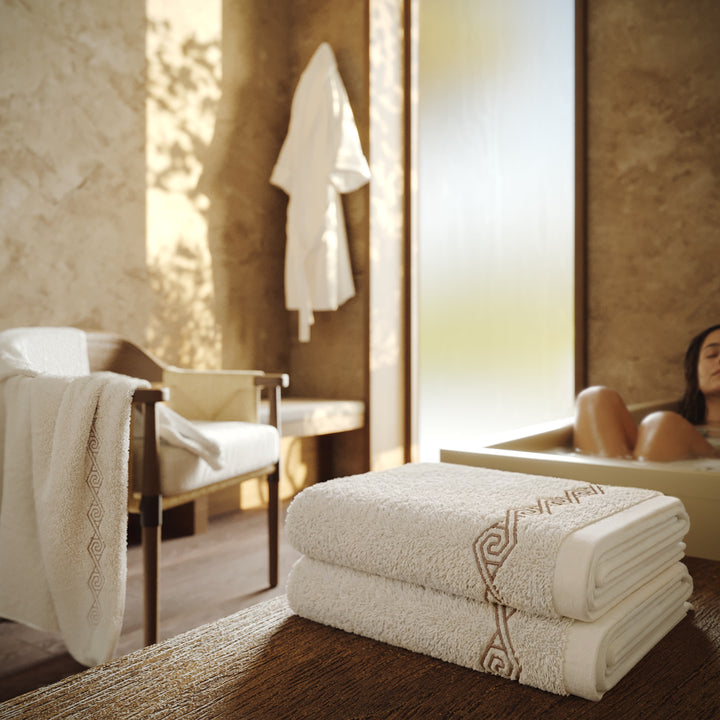 Toallas Senda Bliss blancas con bordado en espiral, presentadas en un baño con luz natural.