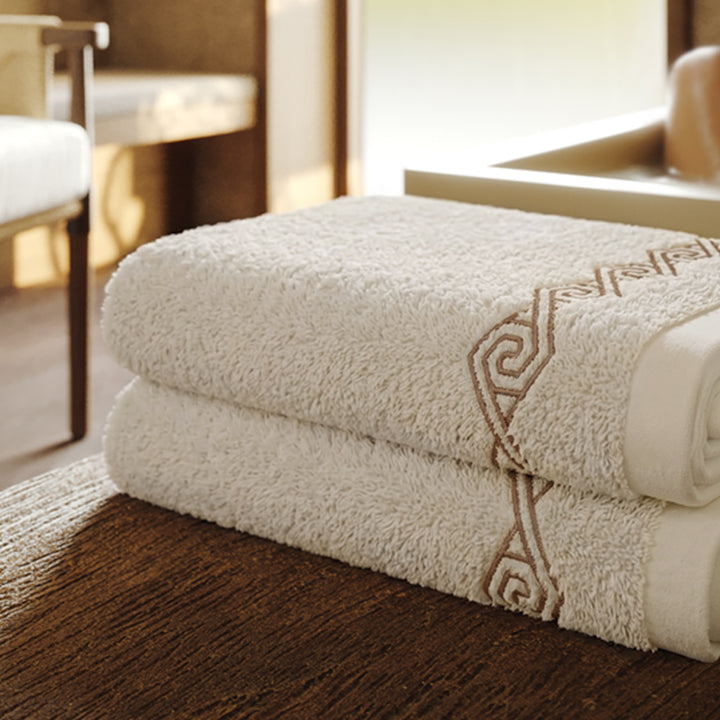 Toallas Senda Bliss blancas con bordado en espiral, presentadas en un baño con luz natural.